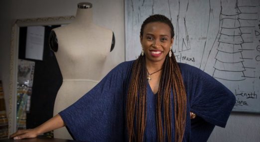 Woman Entrepreneur poses in front of a mannequin and fashion designs