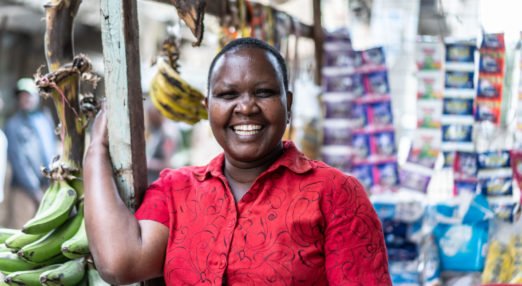 Juliet Kathendu is posing for a portrait next to her small shop where she sells vegetables, and household commodities along the street, Kayole, Kenya.