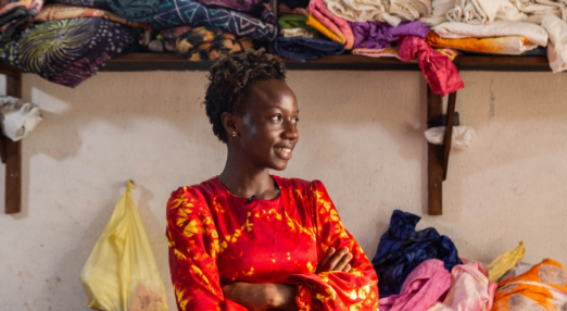 A woman entrepreneur smiles and looks off into the distance in front of a shelf of colourful fabrics