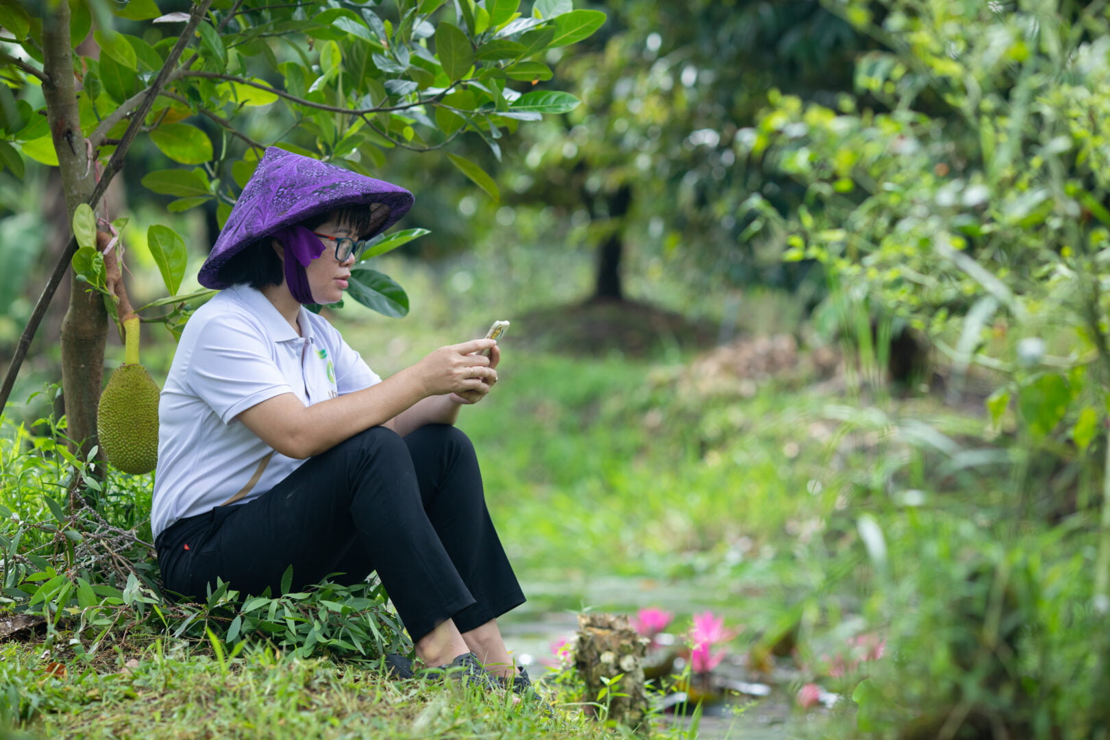 Nguyen Thi Kim Thoa sits in the grass at her farm and uses HerVenture