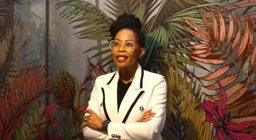 Queen Mokulubete poses in front of colourful palm tree wallpaper at the business where she works.