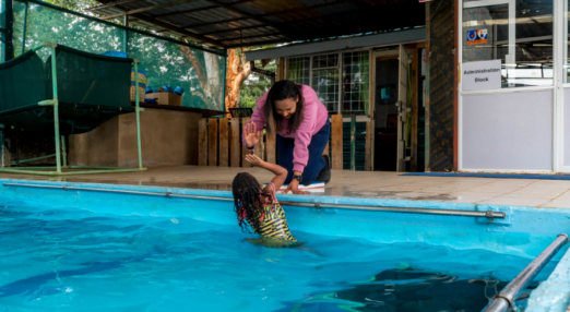 Betty Matharu, Managing Director at Swim Africa in Kenya high fives a young swimming student.