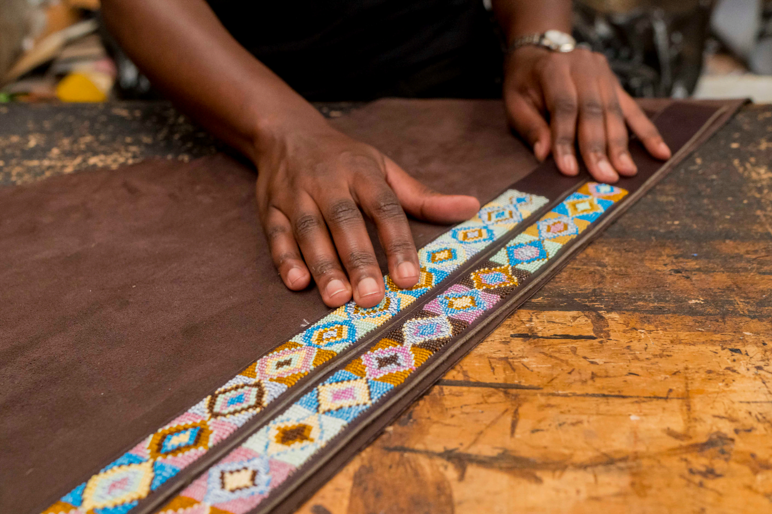 A Kenyan woman entrepreneur's hands rest on top of two leather belts with colourful beading that forms geometric patterns.