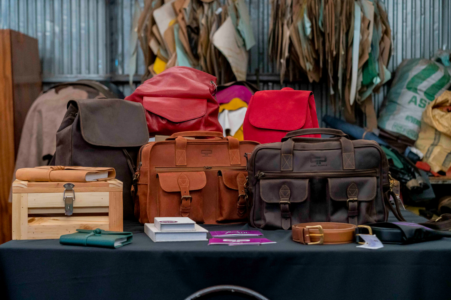 A table with a dark brown backpack, two red leather backpacks, a light brown satchel bag and a dark brown satchel bag.