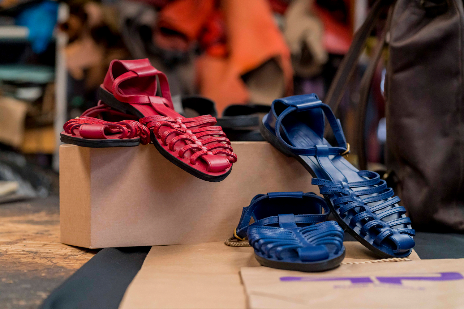 A pair of red leather sandals rests on a box next to a pair of blue sandals.
