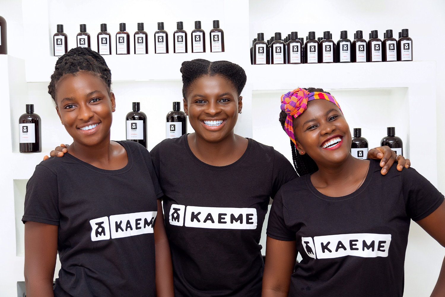 A Ghanaian woman entrepreneur stands between two other Ghanaian women. They are all wearing black shirts with the Kaeme logo.
