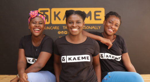 A Ghanaian woman entrepreneur stands between two other Ghanaian women. They are all wearing black shirts with the Kaeme logo.