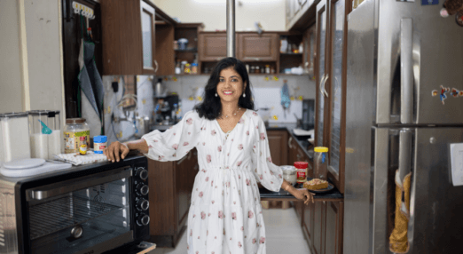 Prachi Robinson, a woman entrepreneur from India stands in the middle of a kitchen. She is smiling at the camera, with one hand resting on an oven and the other on a countertop.